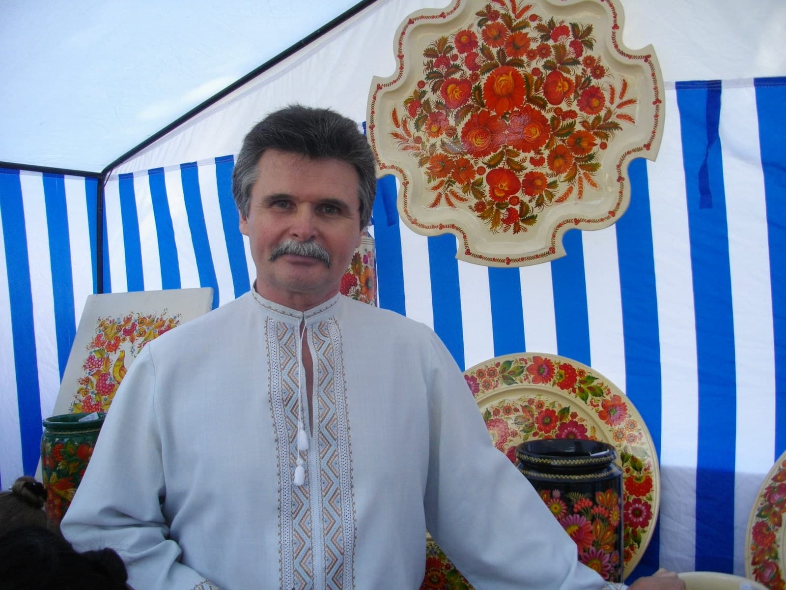 Andrii Pikush in an embroidered shirt among his painted wooden trays and plates